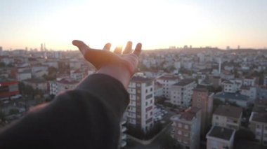 Bir insan elini şehrin üzerindeki canlı günbatımına doğru uzatır..