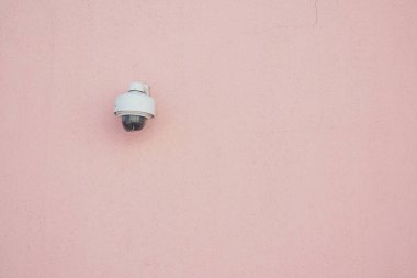 Security camera installed on a soft pink wall offers surveillance support.