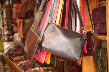 Çeşitli renklerde deri çantalar bir markette ahşap bir vitrinde asılı duruyor..