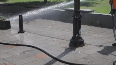 İşçiler kamu parkında kaldırım temizlemek için yüksek basınçlı su kullanıyorlar.