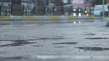 Yağmur yolda su birikintileri oluşturur, alacakaranlıkta şehrin ışıklarını yansıtır..