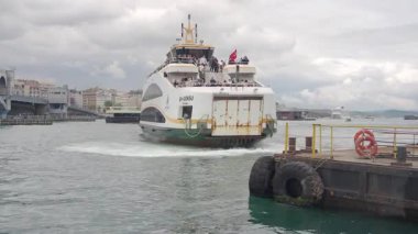 Bir feribot bulutlu gökyüzünün ortasındaki limana doğru gidiyor..