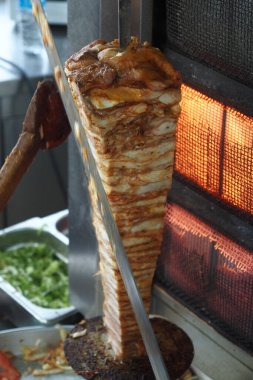 Bir şef, hareketli bir sokakta dikey bir rostodan marine edilmiş eti doğruyor..