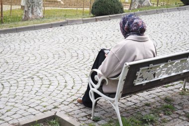 Başörtülü yaşlı kadın parkta huzurlu bir anın tadını çıkarıyor..