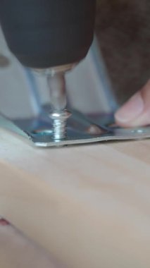 Bir kişi montaj için elektrikli bir alet kullanarak metal bir parantezi tahtaya sabitler..