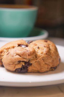 Çikolata parçalı kurabiye, kahve fincanının yanındaki beyaz tabakta duruyor..