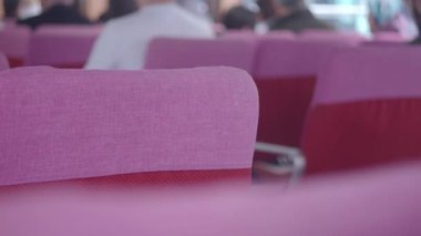 İnsanlar pembe sandalyeli canlı bir bekleme salonunda toplanıyor..