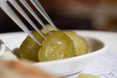Bir çatal, içinde daha fazla turşu olan bir tabaktan bir dilim turşu kaldırır..