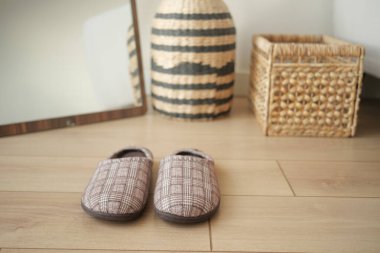 Örülmüş depolama sepetlerinin yanındaki ahşap zemine yerleştirilmiş sıcak terlikler..