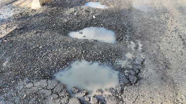 Hasarlı asfalt yol yüzeyinde derin çukurlarda su birikintileri oluşur..