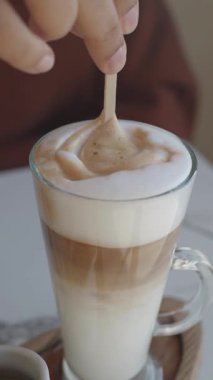 Bir insan cam bardakta köpüklü bir latte karıştırır. 