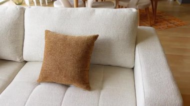 Yumuşak bej kanepe şık bir yaşam alanında sıcak kahverengi bir yastık içerir..