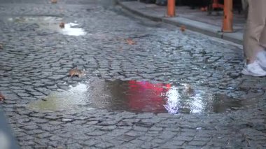 Yağmur yağdıktan sonra kaldırım taşlı bir sokakta su birikintileriyle yürüyen bir insan..