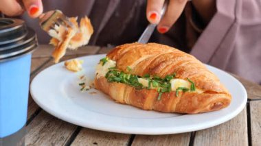 Bir insan ot ve kahveyle dolu taze pişmiş kruvasanın tadını çıkarır..