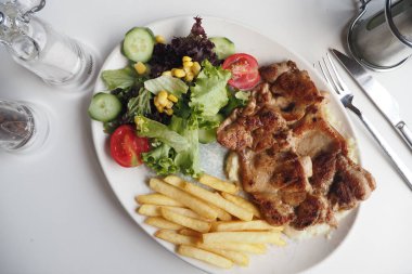 Tabakta ızgara tavuk, salata ve patates kızartması olan lezzetli bir yemek..