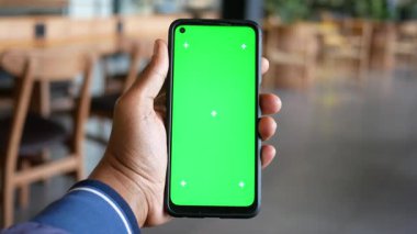 Bir kişi, rahat bir kafede yeşil ekranlı akıllı bir telefon gösterir..