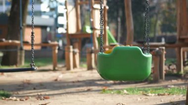 Çocuklar hareketli bir park ortamında salıncaklarda huzur içinde oynarlar..