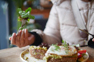 Bir insan kahvaltıda yumurta ve taze yeşilliklerle kaplı avokado tostunu sever..