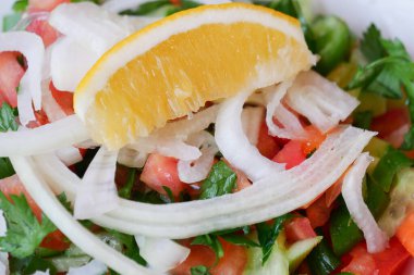 İçinde domates, soğan ve ferahlık için bir dilim limon bulunan renkli salata.