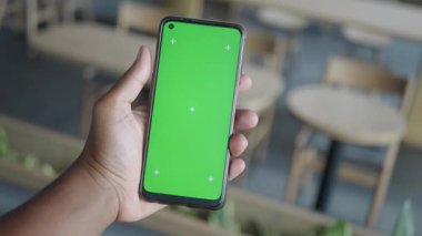 Modern bir kafede canlı yeşil ekranlı akıllı bir telefon sergiliyor..