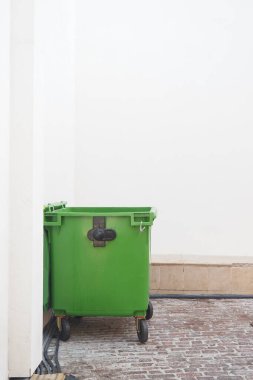 Minimalist bir yerin köşesinde sessizce duran yeşil bir çöp tenekesi..