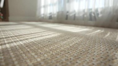 Güneş ışığıyla aydınlık bir oda. Sade bir halının üzerinde desenler oluşturuyor..