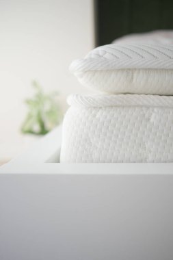 Yumuşak beyaz yatak, parlak bir odadaki ahşap bir çerçeveye düzgünce yerleştirilmiştir..