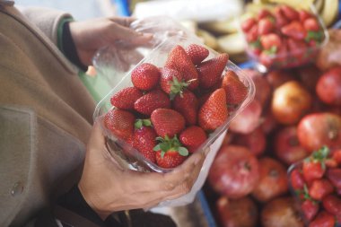 Birisi markette içi olgun çilek dolu bir kap tutuyor..