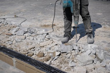 Bir inşaat işçisi, bir proje sırasında kırık kaldırımda kaya matkabı kullanıyor..