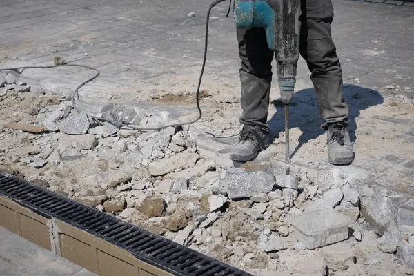 Bir inşaat işçisi, bir proje sırasında kırık kaldırımda kaya matkabı kullanıyor..
