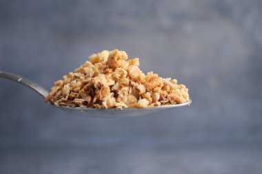 Gümüş kaşığın üzerindeki granola çıtırtısını ve rengini ön plana çıkarıyor..