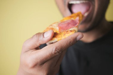 Bir insan rahat bir yerde lezzetli bir dilim pizzadan bir ısırık alır..
