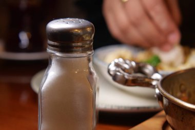 Bir el yemek için uzanırken, bir tuzluk yemek masasında dinlenir..