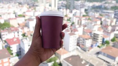 Canlı bir şehir manzarasına bakarken sıcak bir içecek tutmak.