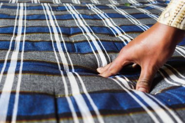 Kişi, dokulu bir yüzey oluşturmak için mavi ve gri çizgili kumaşa basar..