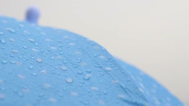 Yağmurda mavi bir şemsiye üzerinde toplanan damlacıkları gözlemliyorum..