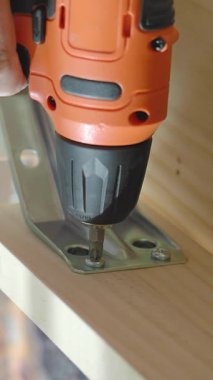 Bir insan, tahta yüzeylere metal parantez kurmak için matkap kullanır..