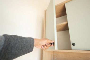 Parlak bir odada bir kişi dolap kapısına uzanır..