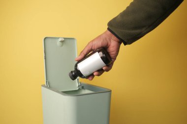 Bir el, yeşil bir çöp kutusuna bir şişe koyar..