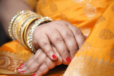 Kırmızı tırnaklı ve altın bilezikli eller parlak turuncu kumaşın üzerinde dinleniyor..