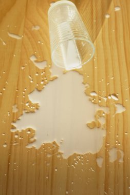  Süt ahşap bir yüzeye döküldü ve plastik bir bardak yakınlarda dinleniyor..