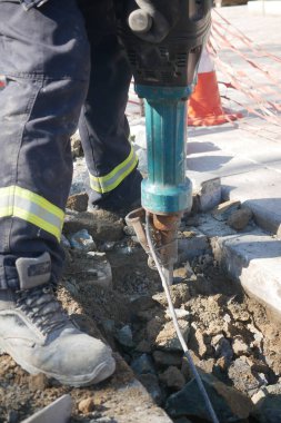İşçi yol onarımı sırasında beton kıran bir matkap kullanıyor..