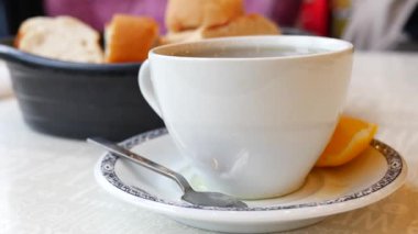 Sıcak bir fincan çay taze ekmek ve bir dilim limon yanında oturur..