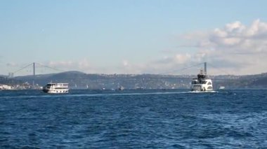 İki tekne bulutlu berrak bir gökyüzünün altında sakin sularda hareket eder..