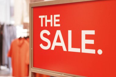 Parlak kırmızı tabela giysi ürünleriyle perakende satış duyurusu yapıyor..