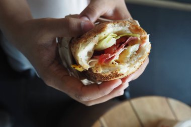 Bir insan kafede içi malzemelerle dolu taze bir sandviç tutar..