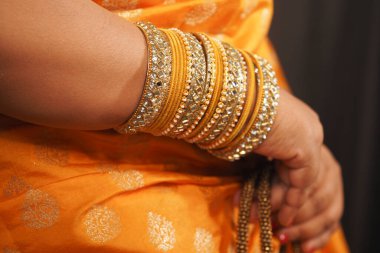 Parlak turuncu kumaş perdeler zarifçe sergilenirken göz kamaştırıcı altın bilezikler.