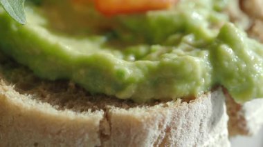 Taze domates dilimli tam tahıllı ekmeğin üzerine serpiştirilmiş lezzetli bir avokadonun tadını çıkarın..