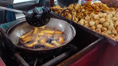 Bir satıcı canlı bir markette çeşitli atıştırmalıklar hazırlar ve kızartır..