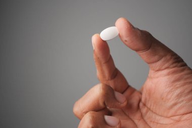 Bir el, arka planda beyaz bir hap tutuyor..